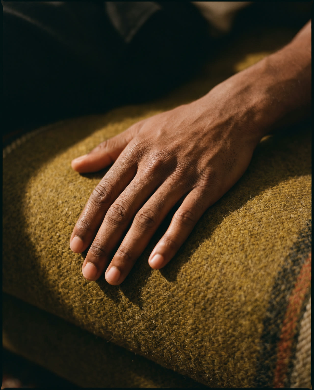 Concept photograph of a hand resting against textured olive wool in warm light.
